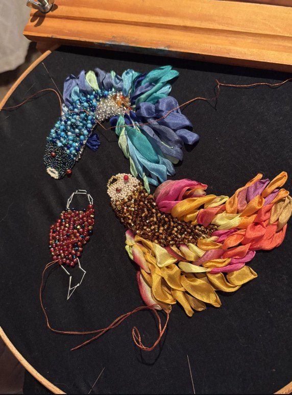 Two small birds worked in beads and coloured silk ribbon on black cloth, partly finished