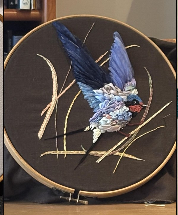 A swallow worked in silk ribbon on dark cloth, still stretched in its wooden embroidery hoop
