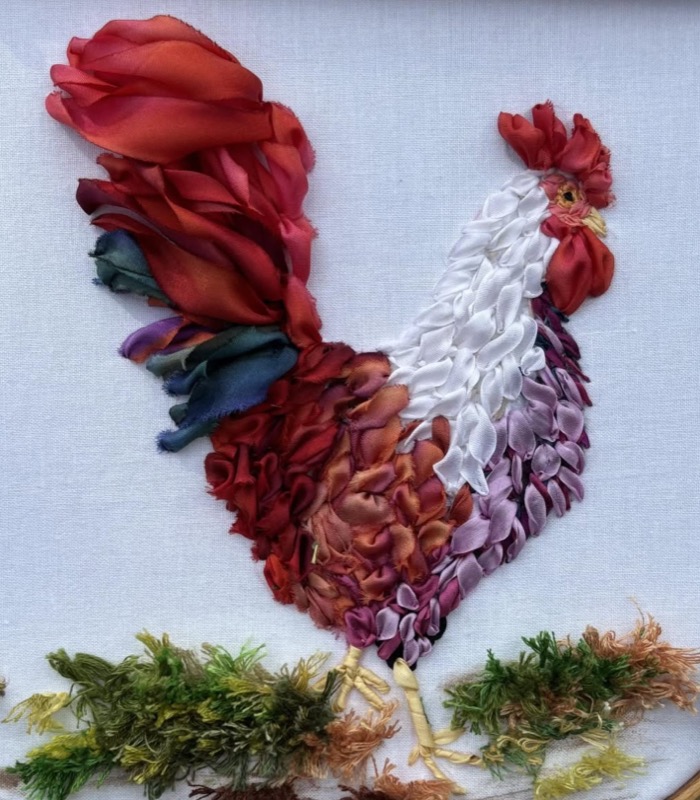 A cockerel in red, orange and lilac silk ribbon, striding through tufted green grass