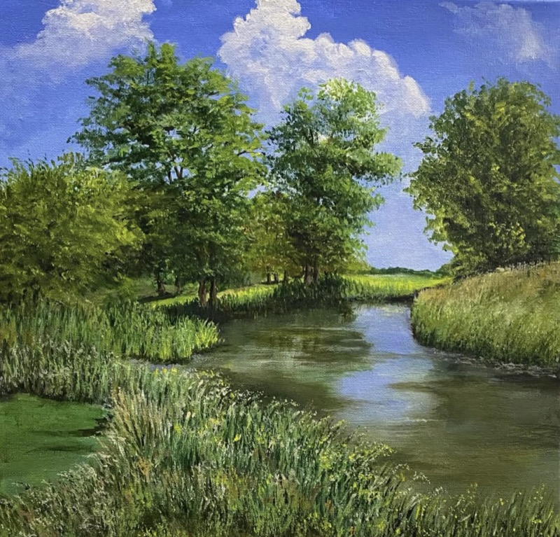 A still river winding between summer trees and tall reeds, under a blue sky with white clouds