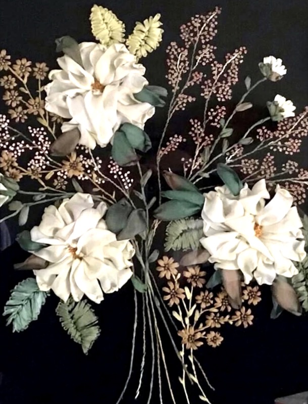 Three cream silk ribbon roses with sprays of small pink and gold flowers, on a black ground